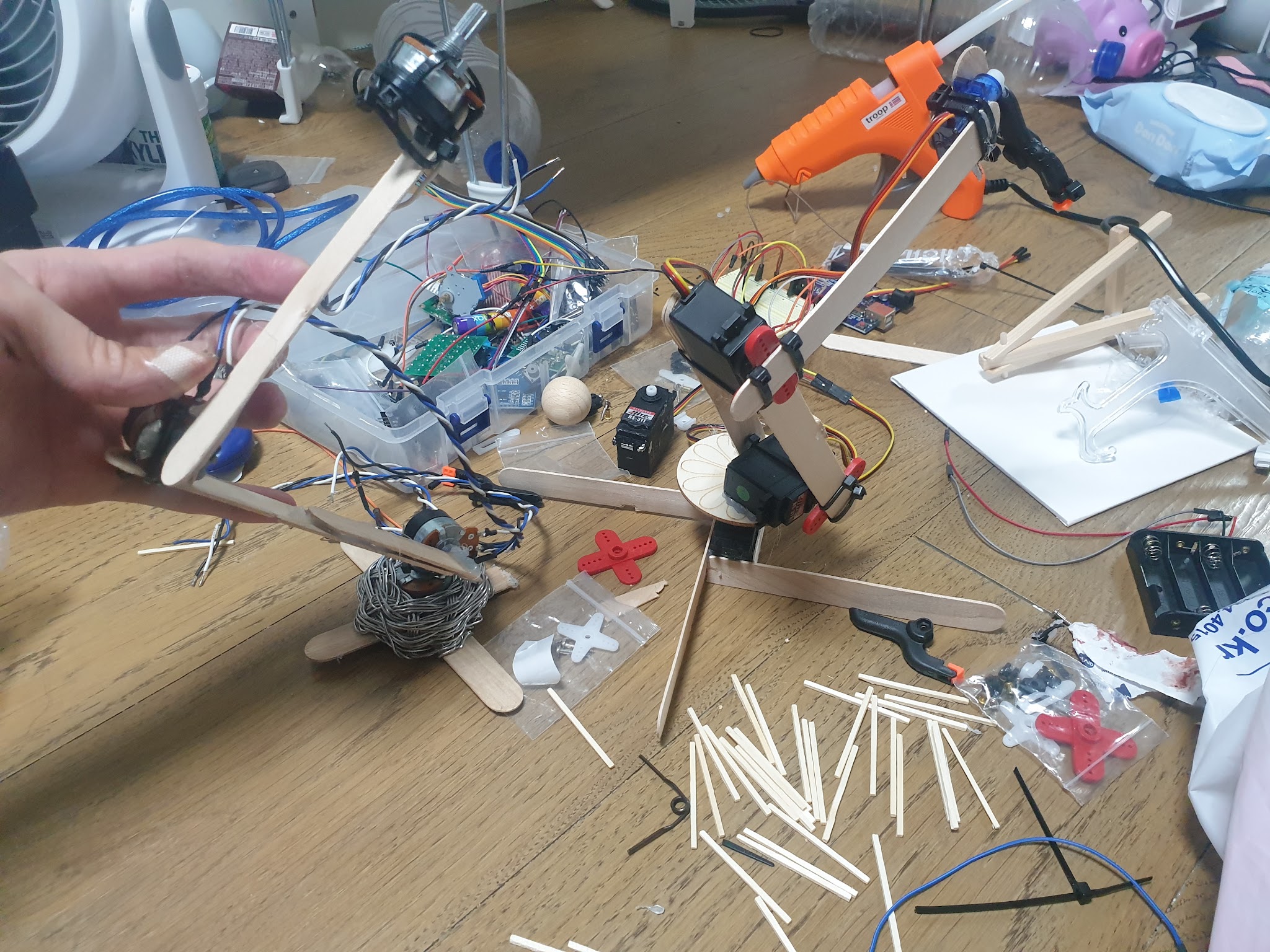 A hand holding the wooden potentiometer dummy arm beside the wired robotic arm